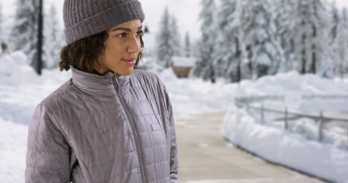 Cute happy black female in winter coat stands outside in the snow looking around