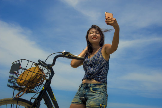 young pretty and happy Asian Chinese girl riding vintage bicycle on the beach taking selfie portrait picture with mobile phone