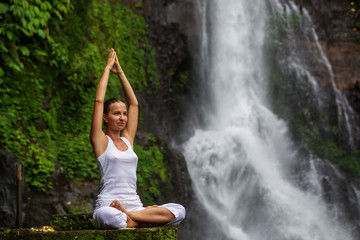Woman practices yoga at Gitgit waterfall on Bali in indonesia