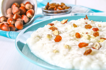 Rice milk porridge with nuts and raisins in a blue dish on a white wooden table.