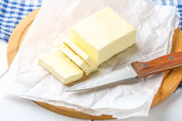 A bar of butter on a wooden board with a knife, on a white table. Ingredients for cooking.