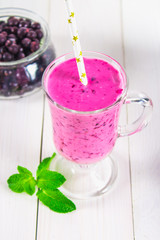 Smoothies of black currant in a glass with a handle on a white wooden table.
