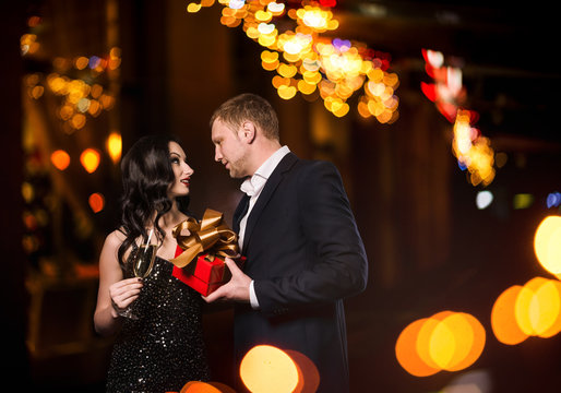 man in suit gives elegant woman a gift box outdoor at night 