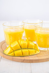 Yellow smoothie of mango, banana and orange on a white wooden table.