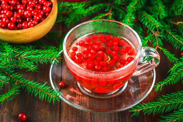Hot tea from cranberries in a glass cup surrounded by fir branches on a wooden table.