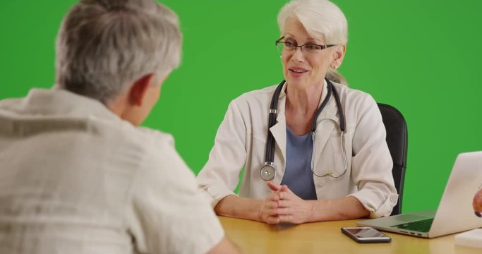 Senior woman doctor talking to elderly patient in the office on green screen. On green screen to be keyed or composited. 