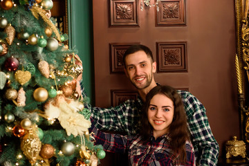 Couple in love next to a Christmas tree, hugging and looking to the camera