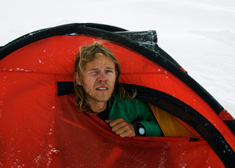 Mountaineer in a red tent on snow in the mountains of Pamir © Natalia