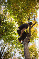 Young man doing a side flip or somersault while practicing parkour on the street with a tree in the background.  