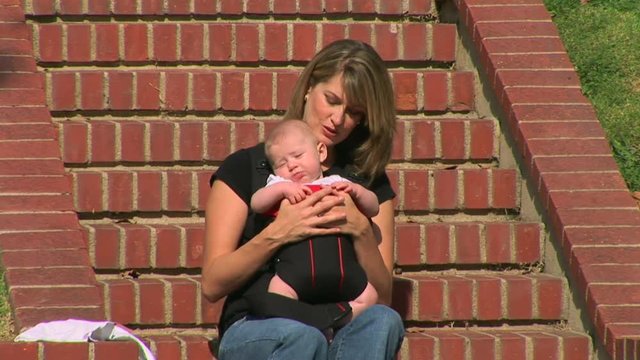 Mother sitting on front steps holding new baby in sling