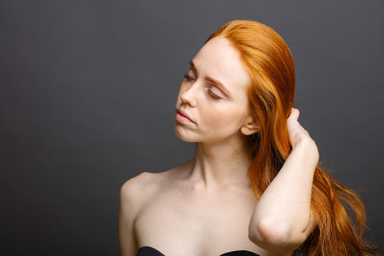 beautiful redhead woman holding her healthy and shiny hair, studio gery
