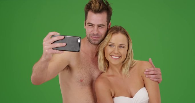 Happy millennial couple taking pictures with smartphone at the beach on green screen. On green screen to be keyed or composited. 