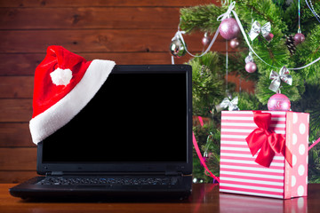 Christmas laptop in santa hat standing on a wooden table, a free space.