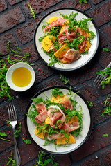 Fototapeta premium Fresh Tasty Persimmon salad with arugula, parma ham, olive oil and herbs. autumn, winter healthy food