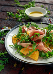 Fresh Tasty Persimmon salad with arugula, parma ham, olive oil, pumpkin seeds and herbs. autumn, winter healthy food