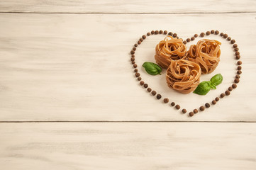 Macaroni in the form of nests with basil in the shape of heart on a white wooden background