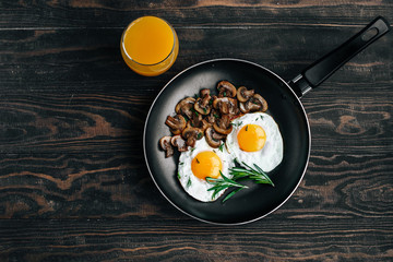 Vegetarian breakfast with fried eggs and mushrooms decorated with a rosemary sprig in a frying pan on a wooden table