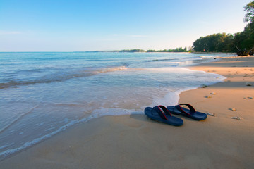 Fototapeta na wymiar Slippers on the beach during early morning at Phuket beach Thailand with very nice weather and clear blue sky with sea water tide 