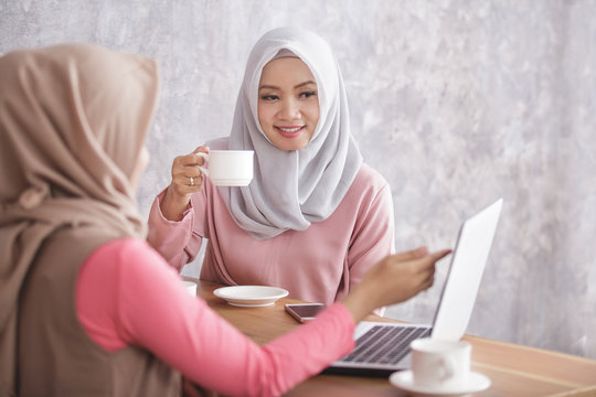 beautiful muslim women explaining project on laptop to her sibli