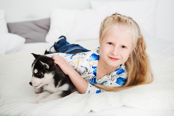 Happy Little girl lying on a bed and hugging with the puppy husky dog