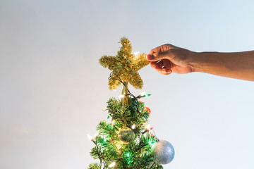 Hand putting sparkling golden star on Christmas tree for decorating and celebration in Christmas Holiday