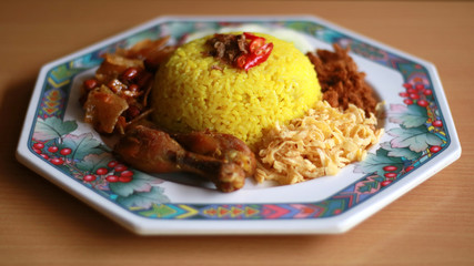 Indonesian turmeric rice or nasi kuning served with fried egg, chicken, and cucumber. Wood background.