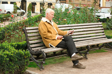 Fototapeta premium Handsome mature man reading newspaper on bench outdoors