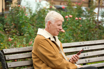 Handsome mature man using phone on bench outdoors