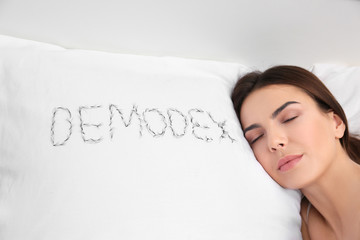 Sleeping woman and word "Demodex" written with artificial eyelashes on pillow