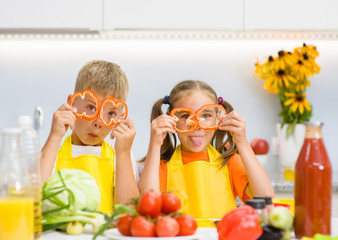 Funny children having fun with food vegetables at kitchen holds pepper before his eyes like in glasses