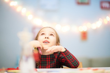 Surprised little girl looking upwards with interest while distracted from drawing Christmas card...