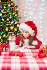 Little girl in red christmas hat writes letter to Santa Claus