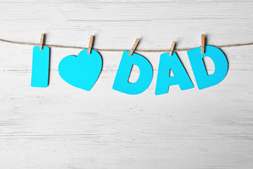 Phrase "I love dad" made of paper letters as greeting for Father's day on string against wooden background