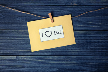Card with phrase "I love dad" for Father's day on string against wooden background