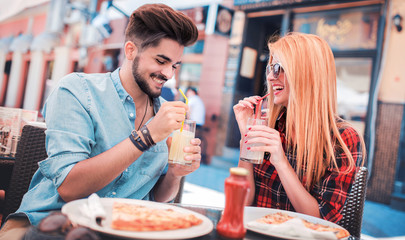 Beautiful young couple sitting in the cafe and eating pizza. Consumerism, food, lifestyle concept