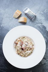 Risotto with chanterelle mushrooms served in a white plate over grey concrete background, vertical shot, view from above