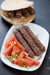 Barbecued balkan cevapi or cevapcici sausages with red tomatoes, onion and pita bread, vertical shot