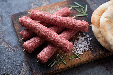 Closeup of a wooden chopping board with raw balkan cevapi or skinless beef sausages on skewers, selective focus
