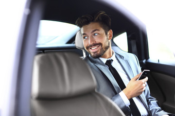 Unsmiling businessman sitting in the back seat in his car