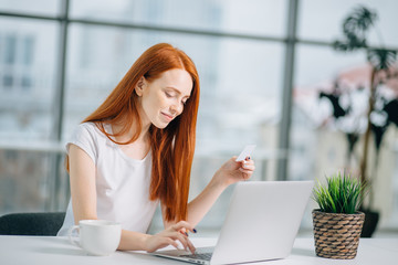Close up of a happy redhead woman hand buying online with a laptop and paying with a credit card