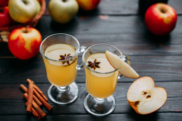 Two glasses of hot and spicy apple cider decorated with anise and apple slice on dark wooden table. Delicious warming winter beverage
