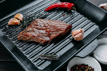 Appetizing beef steak with rosemary, chili pepper, garlic and spices on the grill pan. Restaurant kitchen, cooking concept