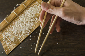 chopsticks in hand in the background of a sushi mat and scattered rice