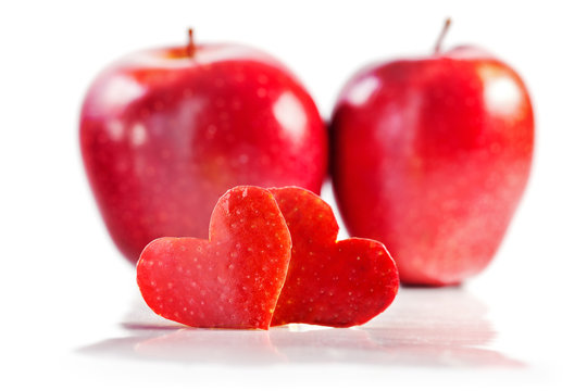 Two red hearts are cut out from apple, two red apples on a background