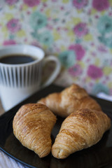 Cropped, close-up shot of breakfast with three croissants and large black coffee in an old-fashioned style setup, with copy space and selective focus