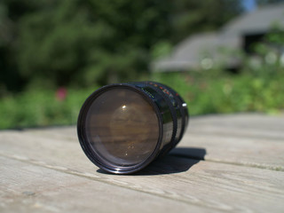 Vintage camera lense on wooden boards with plants in the background - pictured from the side