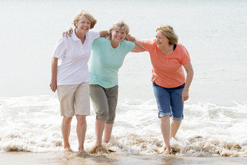 group of three senior mature retired women on their 60s having fun enjoying together happy walking on the beach smiling playful