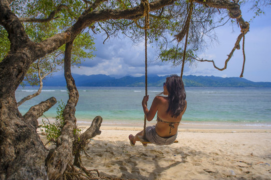 young beautiful Chinese Asian girl having fun on beach tree swing enjoying happy feeling free in Summer holiday tropical trip