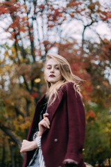 portrait of a luxurious, beautiful, young girl. Dressed in stylish clothes, walking in an autumn park. Bright lipstick on the lips.