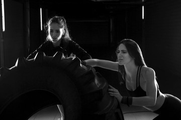 Fototapeta na wymiar Strong young girls exercise with big tractor tire in gym